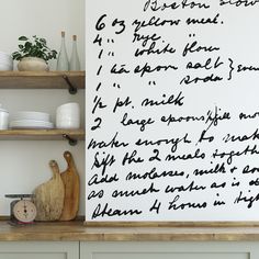 a kitchen wall with writing on it next to some dishes and utensils in front of a wooden shelf