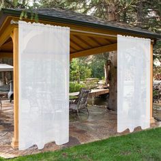 a covered patio area with chairs and tables in the background, surrounded by grass and trees