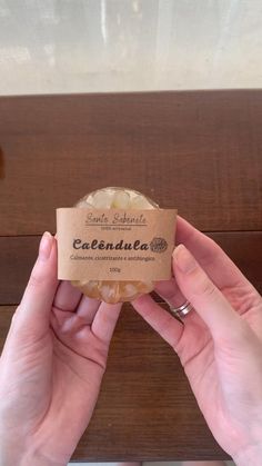 two hands holding a soap bar in front of a wooden table with a sign on it