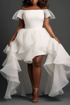 a woman wearing a white dress with ruffled skirt and high heels standing in front of a gray background