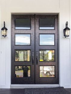 the front door to a home with two lights on each side and an entrance mat