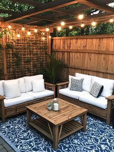 an outdoor living area with couches, tables and lights on the side of the fence