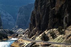 there is a train going down the tracks in the mountains near some water and rocks