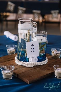 a table topped with candles and water filled glass vases covered in seaweed on top of a wooden board