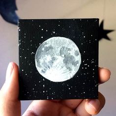 a hand holding up a small card with the moon painted on it