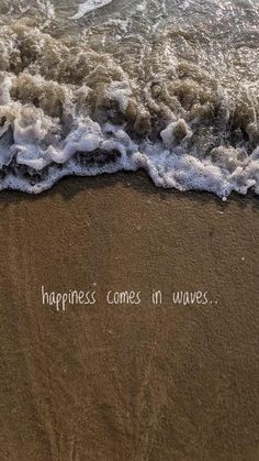 the words happiness comes in waves written on the sand at the ocean's edge