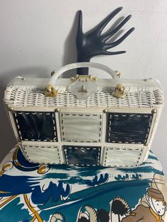 Stylecraft of Miami is one of my favorite handbag designers! Their range of styles were very vast. This purse is very stylish in white wicker with white and gray pearlized Lucite squares that are stitched on in contrasting stitching. There are a few broken stitches but it does not detract from the beauty of this purse. It sits on 4 brass feet. The Lucite turn lock closer opens to reveal a clean white vinyl interior with one zippered pocket and the original tag. The purse measures 8X12X3.5 with the Lucite handles adding 4.5". EUC Designer Rectangular Straw Bag With Braided Handles, White Handheld Straw Bag With Braided Handles, Designer White Square Bags, White Woven Handheld Straw Bag, Designer White Rectangular Case Bag, Designer White Square Bag, White Rectangular Shoulder Bag Gift, Handheld White Woven Straw Bag, White Rectangular Case Shoulder Bag For Shopping