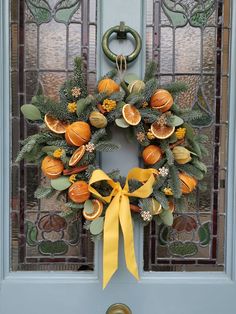 a wreath on the front door with oranges and green leaves hanging from it's side