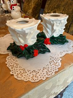 two white candlestick holders sitting on top of a doily covered table with holly and red berries