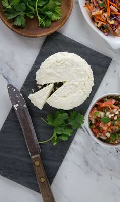 a cutting board topped with cheese next to bowls of salads and a large knife