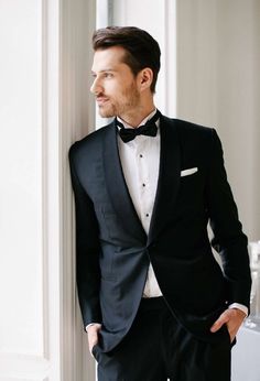 a man in a tuxedo leaning against a wall