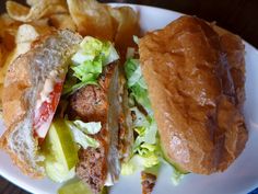 a white plate topped with a cut in half sandwich next to potato wedges and chips