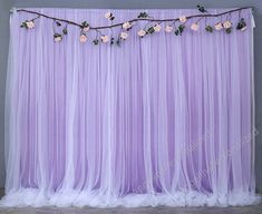 a purple backdrop with flowers and vines hanging from the top, along with white tulle curtains