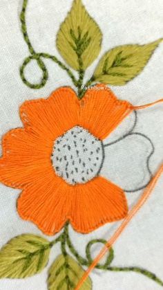 an orange flower with green leaves is on the white fabric, which has been stitched onto it