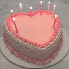 a pink heart shaped cake with candles on it's top and white frosting