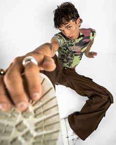 a young man is pointing his finger at the camera while wearing brown pants and a green shirt