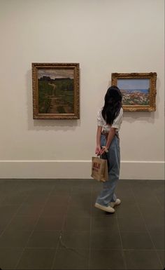 a woman standing in front of two paintings on display at an art gallery, with one holding a shopping bag and the other looking down