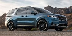 a blue suv parked on the side of a road in front of mountains and clouds