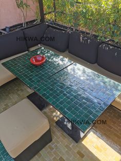 an outdoor table and bench with green tiles on the floor, surrounded by potted plants