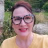 a woman wearing glasses is smiling for the camera while standing in front of some trees