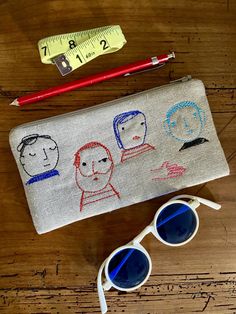 a pencil case sitting on top of a wooden table next to sunglasses and a ruler