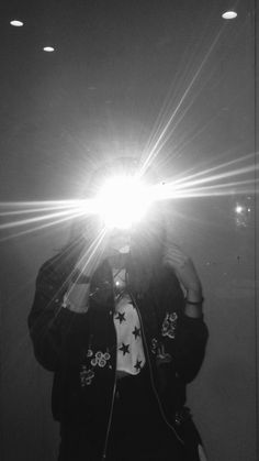 black and white photograph of person taking selfie with light shining through the window behind them