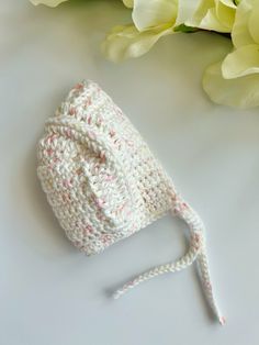 a white crocheted hat sitting on top of a table next to some flowers