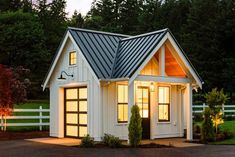 a small white house with a metal roof and two windows at night in the evening