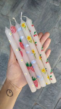 four white candles with strawberries and daisies on them are held in a hand