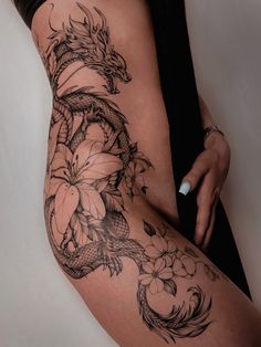 a woman's thigh with a dragon tattoo and flowers on the side by her