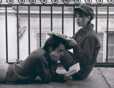 two people sitting on the ground with books in their hands and one person laying down