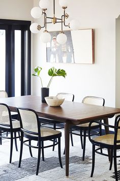 a dining room table with chairs and a bowl on it's centerpiece in front of a large window