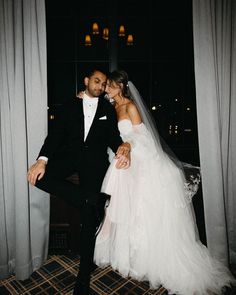 a bride and groom posing for a photo in front of a window at night time