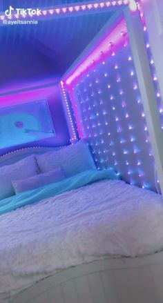 a bed with white sheets and blue lights on the headboard is in a room