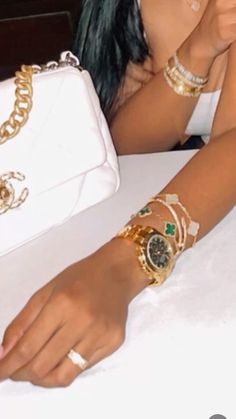 a woman sitting at a table with two bracelets on her wrist and a purse behind her