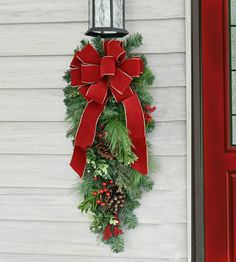 a christmas wreath hanging on the side of a house with a lantern and pine cones