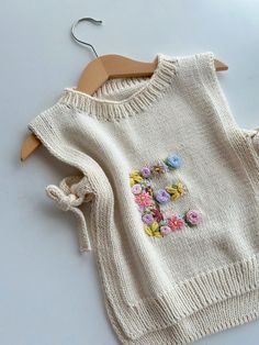 a white sweater with flowers on it and a wooden hanger