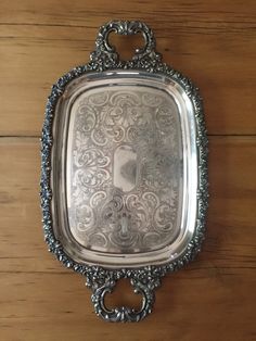 an ornate silver tray with handles on a wooden surface, resting against a wall or floor