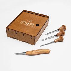 a wooden box with three knives in it next to another set of knifes and a sharpener