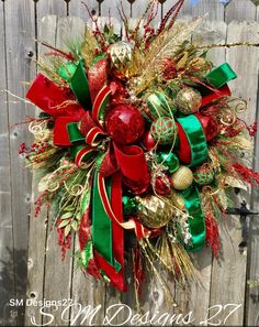 a christmas wreath with red, green and gold ornaments hanging on a wooden fence in front of a house