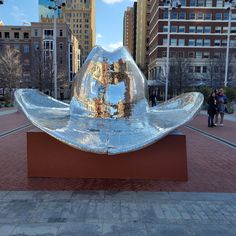 a large metal object sitting on top of a brick walkway in front of tall buildings