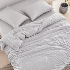 an unmade bed with grey and white striped comforter, pillows and throw blanket