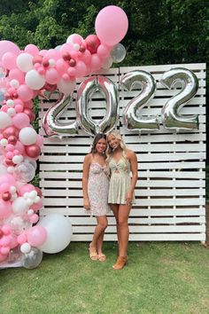 two women standing next to each other in front of a sign with balloons on it