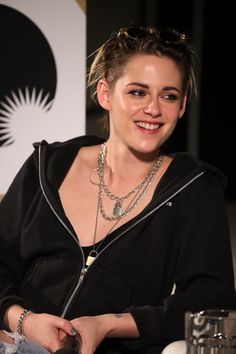 a woman sitting at a table with a drink in her hand and wearing a necklace