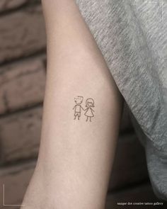 a small tattoo on the arm of a person with a little boy and girl drawn on it