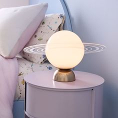 a white lamp sitting on top of a night stand next to a bed with pillows