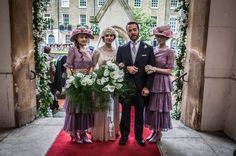 a man and two women standing on a red carpet in front of an archway with flowers