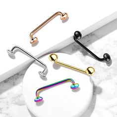 two piercings with different colors on them sitting on a white surface next to a pair of black and gold barbells