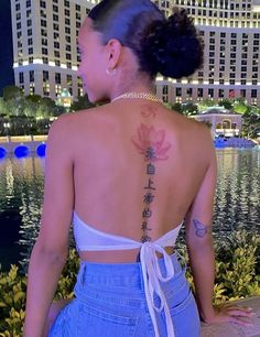 a woman with a tattoo on her back standing in front of a body of water