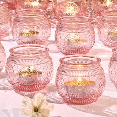 many pink glass candles are lined up on the table